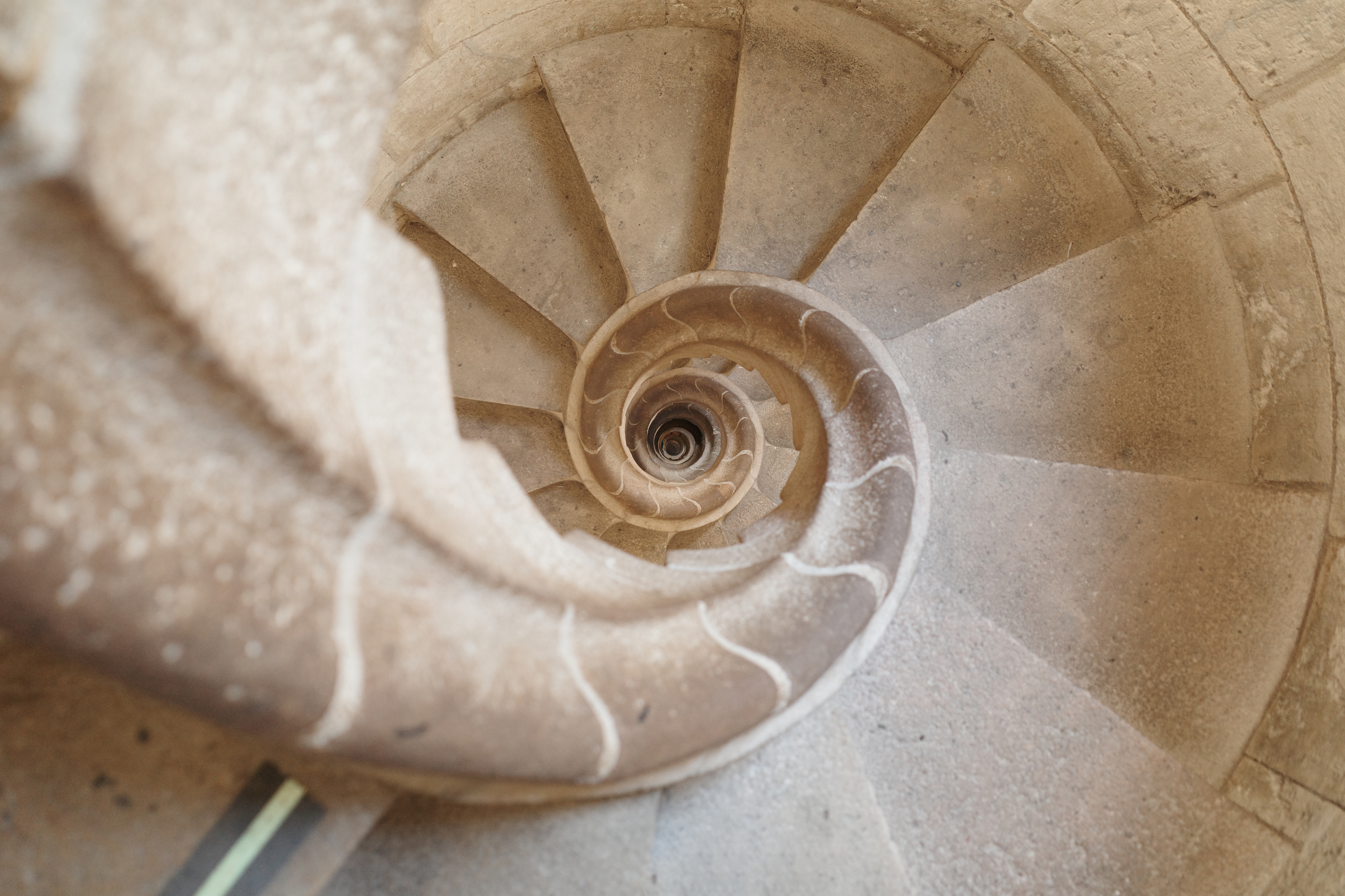 A stone spiral staircase viewed from above, its rings narrowing toward a centre, representing the circles of proximity to institutional power